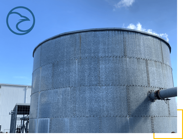 A large industrial storage tank with a pipeline connected on the side under a clear blue sky.